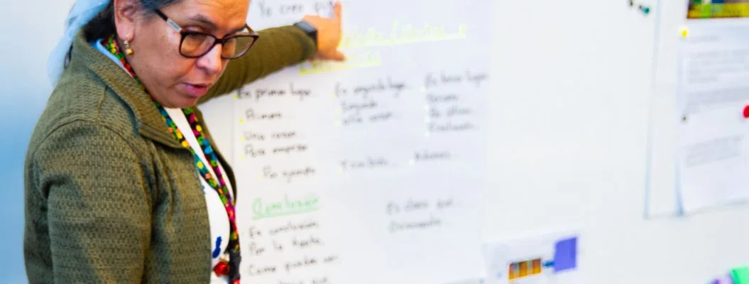 Teacher pointing at whiteboard with written lesson content and colorful charts during classroom instruction.