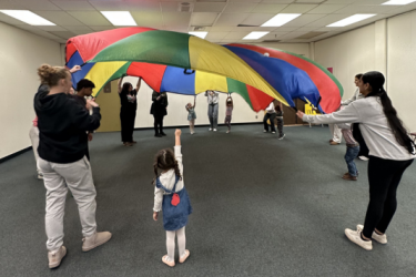 Students and preschoolers playing with a parachute