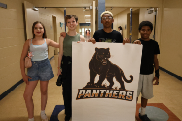 Students standing by a sign with a panther logo on it